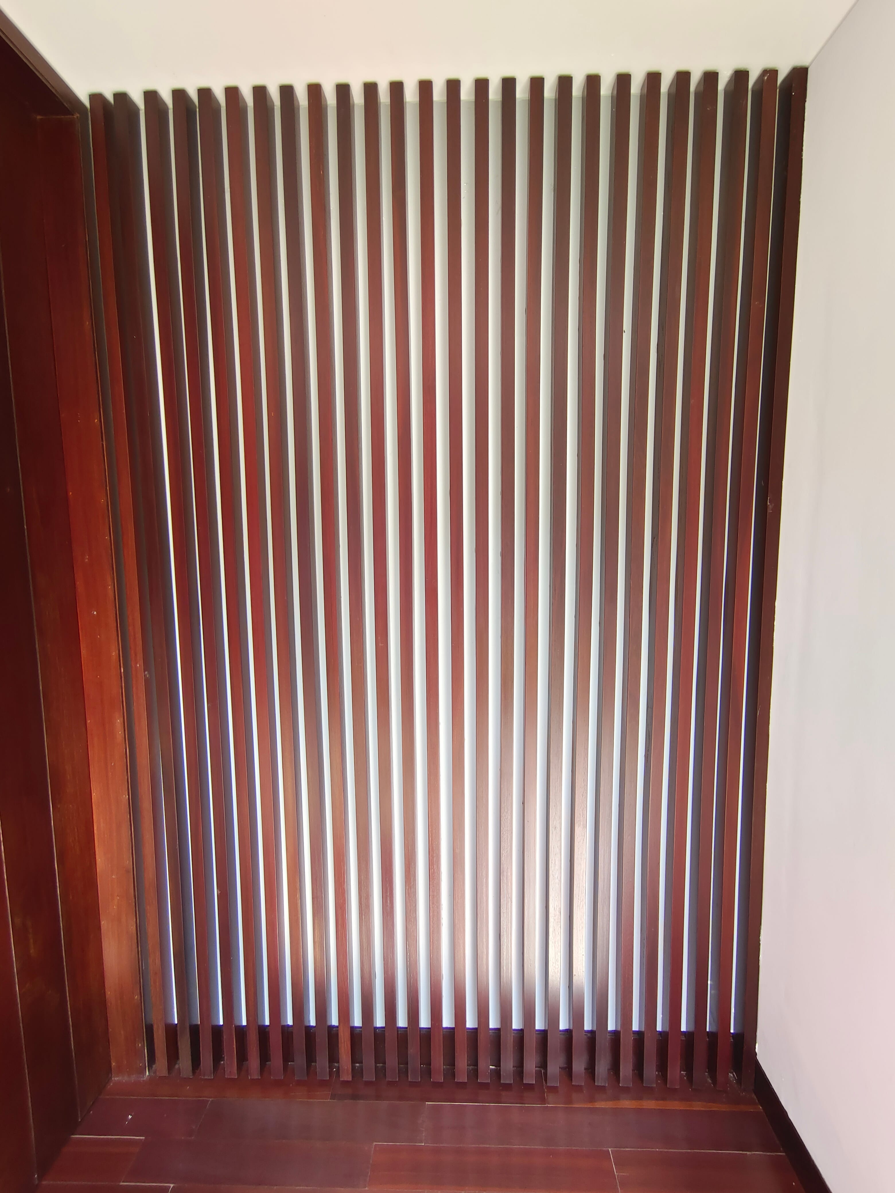 Close-up of interior full-height kisi-kisi wall panel with dark hardwood flooring at Kowi Bangka by Reywood